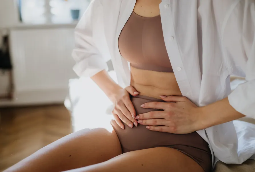 A woman sitting on a bed with both hands resting on her lower belly